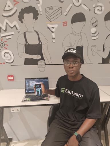David Baiye in front of a mural holding a phone in a workspace.